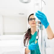 A healthcare professional from Infusions By Boss, wearing blue gloves and a stethoscope, adjusts an IV drip in a bright, clean medical setting—delivering expert IV Infusion Therapy Brisbane can trust.