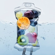 A clear IV bag from Infusions By Boss is filled with water and assorted fresh fruits—kiwi, orange slice, grapes, blueberries, and apple—submerged halfway in water, showcasing the refreshing essence of IV Infusion Therapy Brisbane.