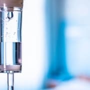 Close-up of an intravenous (IV) drip chamber with clear fluid and air bubbles, set against a blurred blue and white background, highlighting the professional care offered by Infusions By Boss IV Infusion Therapy Brisbane.